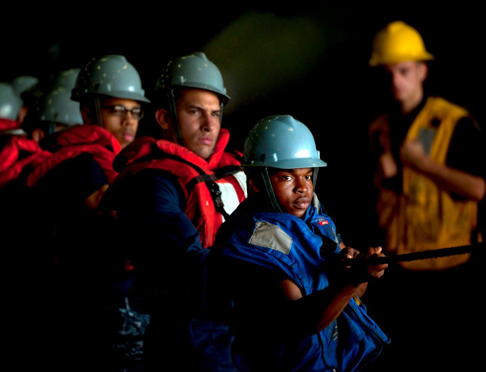 US Navy 110504-N-DR144-321 Seaman Jerrell Merren and other line handlers maintain tension on a line in the hangar bay of the Nimitz-class aircraft