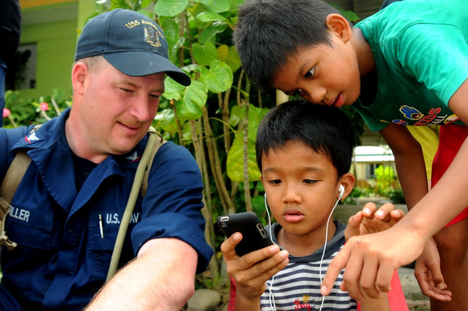 US Navy 110506-N-SP676-176 Mineman 3rd Class Matt Miller gives children his smart phone to play with at the Bukit Harapan home for disabled and dis