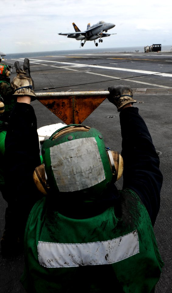 US Navy 110509-N-OY799-051 Aviation Boatswain's Mate (Equipment) Airman Nate Strickland looks on as an F-A-18C Hornet lands aboard USS John C. Sten