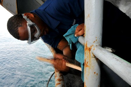 US Navy 110512-N-1004S-248 Boatswain's Mate Seaman Jermia Millsap uses a wire brush to scrape rust from a deck fitting during a planned maintenance