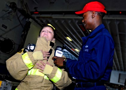 US Navy 110515-N-3154P-255 Damage Controlman Fireman Jameal Defreitas assists a civilian embarked for a Tiger Cruise in putting on fire fighting eq