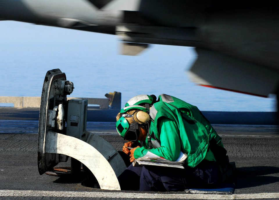 US Navy 110518-N-SB672-102 Aviation Boatswain's Mate (Equipment) Airman Troyphilip Obuga, from Morgantown, W.Va., ducks behind the center-deck hatc