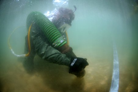 US Navy 110520-N-VF350-023 Navy Diver 2nd Class Joshua Westman sucks sand off the bottom of the ocean during a Joint POW-MIA Accounting Command (JP