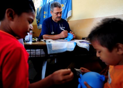 US Navy 110523-N-QD416-239 Capt. Jose Sanchez makes an elephant out of a pair of surgical gloves for two young patients during Continuing Promise 2 photo