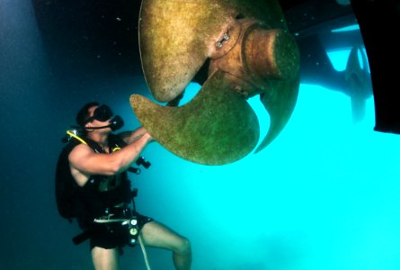US Navy 110609-N-XD935-137 Navy Diver 3rd Class Bryan Myers, assigned to Mobile Diving and Salvage Unit (MDSU) 2, maneuvers around a ships propelle