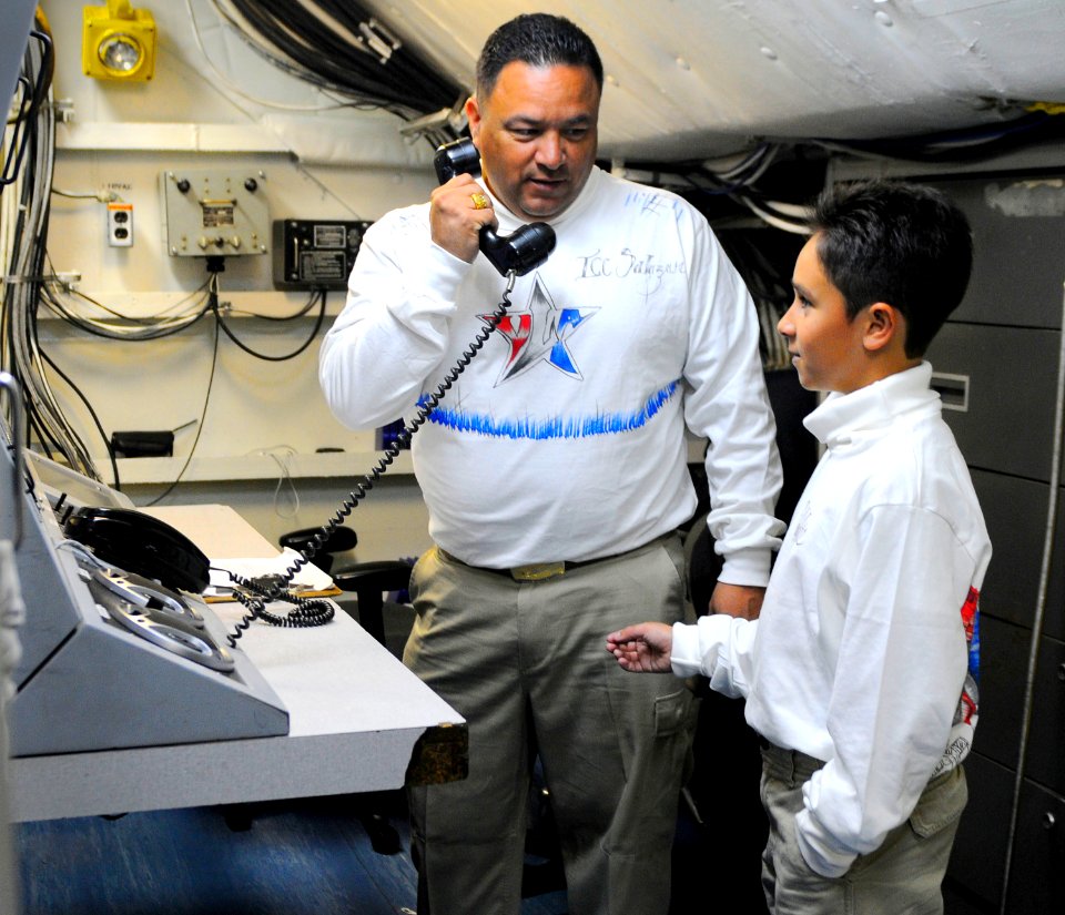 US Navy 110610-N-OK922-318 Chief Interior Communications Electrician Julio Salazar explains the equipment he works with to his sponsored tiger crui