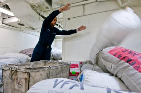 US Navy 110608-N-BT887-303 Aviation Structural Mechanic Airman Justin Sams tosses a bag of clean laundry into a pile in the laundry room aboard USS
