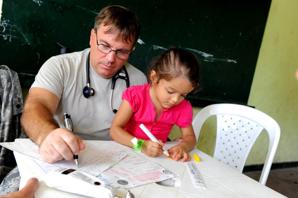 US Navy 110609-F-ET173-228 Maj. Gary Ruesch completes medical forms as his patient draws a picture at the Escuela Max Seidel medical site in Tumaco