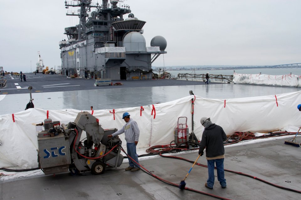 US Navy 110610-N-ZC343-460 Subcontractors for National Steel and Shipbuilding Company (NASSCO) resurface the flight deck of the amphibious assault