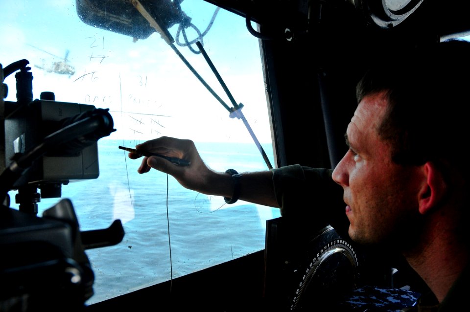 US Navy 110627-N-ZZ999-005 Lt. Jeremiah Harkema marks off pallets on a window in the flight control tower as a MH-60S Sea Hawk helicopter flies ne