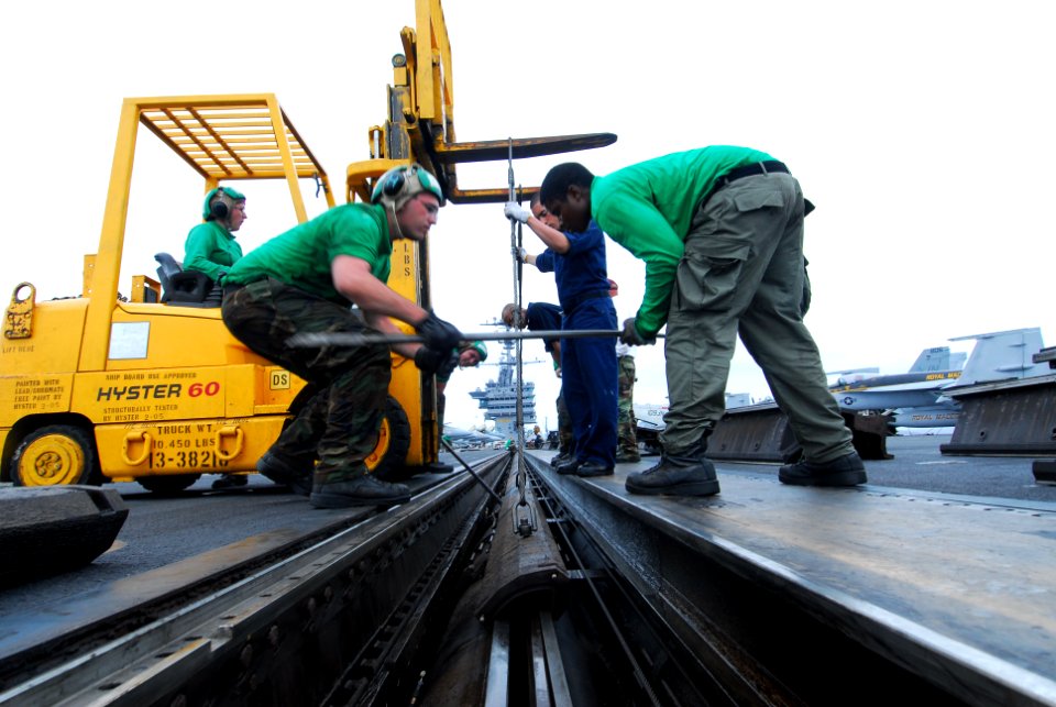 US Navy 110626-N-AW206-005 Aviation Boatswain's Mate (Equipment) Airmen Matthew Sims, left, and Kevin Graves replace sealing strips on one of the c