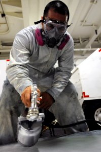 US Navy 110625-N-XE109-553 Aviation Support Equipment Technician 2nd Class Vincente Castillo spray paints the hood of a tractor aboard USS George H