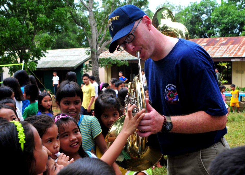 US Navy 110701-N-XR557-175 Musician 2nd Class Anthony Smouse interacts with children at Santa Lourdes Elementary School while playing his french ho