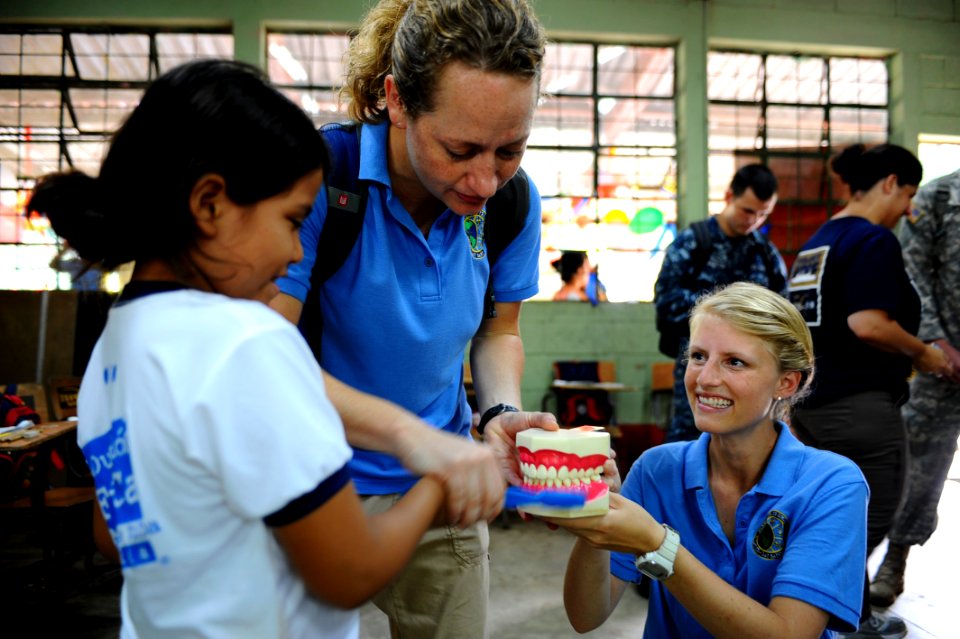 US Navy 110707-F-CF975-147 Nikki Broby and Courtney Lenberg, Latter-day Saint Charities volunteers, demonstrate proper dental hygiene to a student