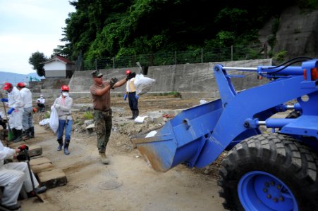 US Navy 110714-N-KK192-053 Construction Electrician 1st Class Joshua Thonissen tosses a mud filled bag into the scoop of a front loader