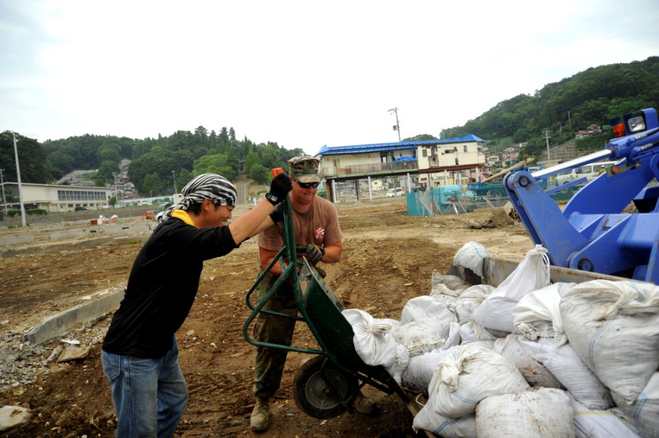 US Navy 110714-N-KK192-128 Construction Electrician 1st Class Joshua Thonissen and a Japanese volunteer load bags of mud into the scoop of a front