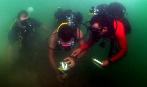 US Navy 110728-N-XD935-136 Chief Hospital Corpsman Nathanael Warren, left, Antonio Sosa and Joni Paniagua find an inert training mine on the sea fl