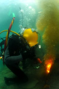 US Navy 110804-N-XD935-475 Petty Officer Darin Atkinson uses an underwater cutting tool to cut through a steel beam during welding operations