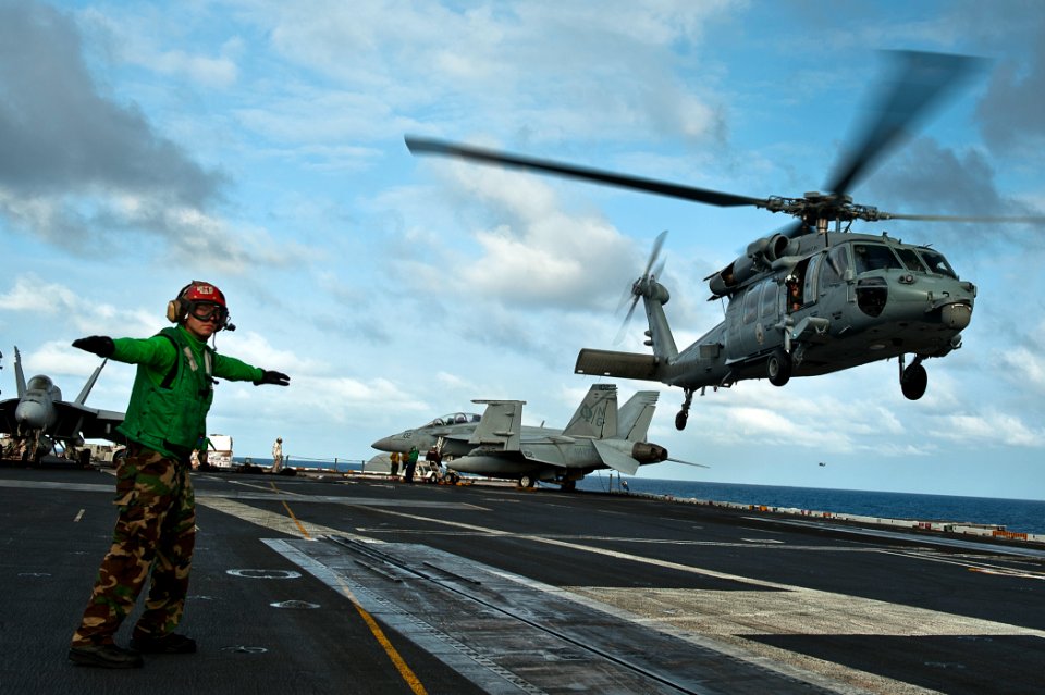 US Navy 110808-N-BT887-104 Aviation Electrician's Mate 3rd Class James Kirby checks the flight deck and airspace before signaling to an MH-60S Sea