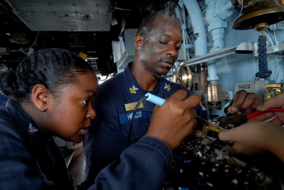 US Navy 110809-N-DU438-265 Electrician's Mate 3rd Class Rashan Ferguson, left, and Chief (Select) Electrician's Mate Dale Holder solder wires in a
