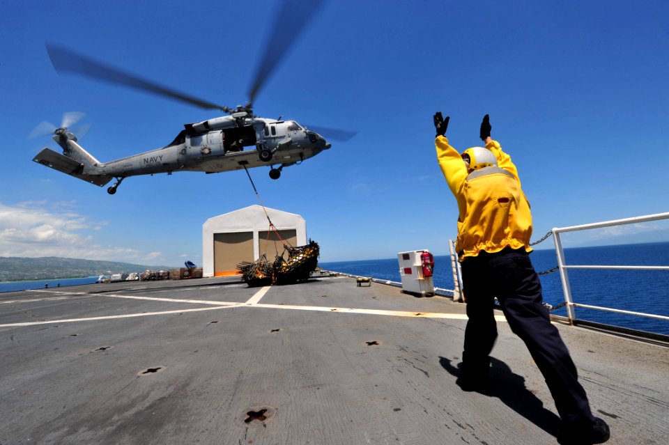 US Navy 110818-F-NJ219-064 A Sailor guides an MH-60S Sea Hawk helicopter toward a pallet of supplies