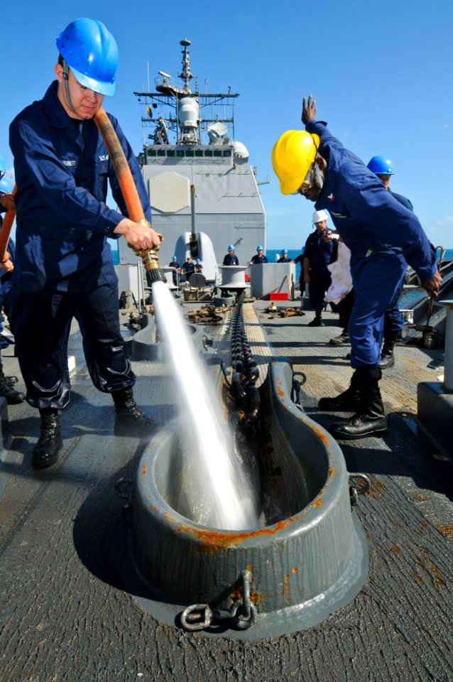 US Navy 110822-N-YM590-027 Seaman Apprentice Todd McBurnett Jr., left, uses a fire hose to clean debris off the anchor chain aboard the guided-miss