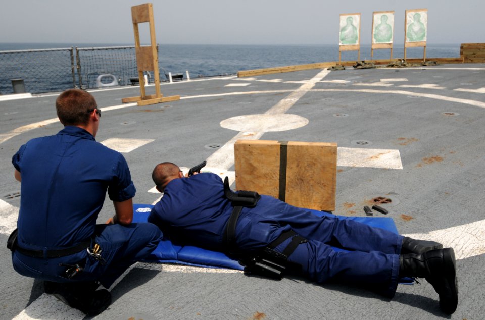US Navy 110905-N-XQ375-489 Gunner's Mate 2nd Class Travis Kaizen watches as Interior Communications Electrician 1st Class Kenny Carriel fires a 9mm