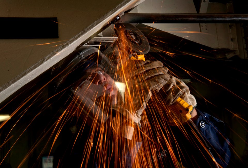 US Navy 111004-N-DR144-256 Hull Maintenance Technician 3rd Class Robert Garcia grinds a weld smooth after installing a length of pipe for a securit