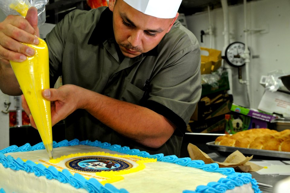 US Navy 111013-N-YM590-093 Culinary Specialist 2nd Class Daniel Lowen decorates a cake for the U.S. Navy's 236th birthday celebration aboard the gu