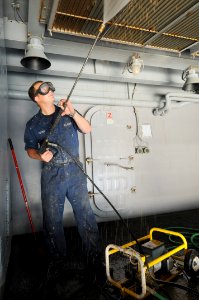 US Navy 111015-N-JD217-020 Seaman Daniel I. Porter pressure washes the overhead on a boat davit aboard the aircraft carrier USS George H.W. Bush (C