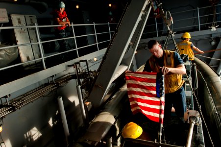 US Navy 111030-N-BT887-256 Boatswain's Mate 2nd Class Alex Armour secures the national ensign on a rigid hull inflatable boat aboard the Nimitz-cla