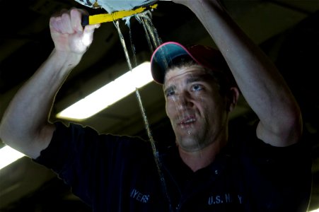 US Navy 111027-N-ZC343-745 Hull Technician 2nd Class John Myers removes the lagging from a ruptured pipe in the upper vehicle storage deck