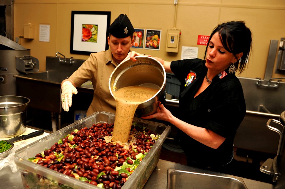 US Navy 111101-N-YR391-069 Celebrity chef Sarah Simington instructs Culinary Specialist 2nd Class Jamie Hartje how to prepare her signature salad