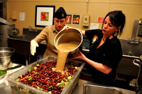 US Navy 111101-N-YR391-069 Celebrity chef Sarah Simington instructs Culinary Specialist 2nd Class Jamie Hartje how to prepare her signature salad photo