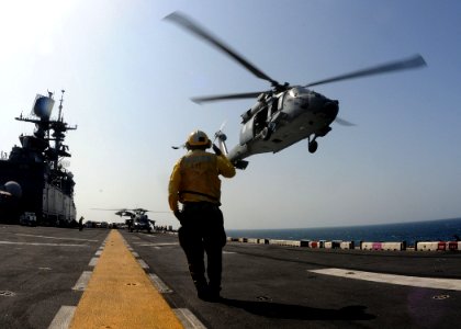 US Navy 111110-N-EC658-010 A landing signalman enlisted salutes an MH-60S Sea Hawk helicopter on the flight deck of the amphibious assault ship USS