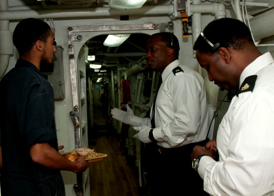 US Navy 111124-N-ER662-089 Senior Chief Fire Controlman Jermain Whitfield, middle, welcomes sailors to the galley aboard the Arleigh Burke-class gu