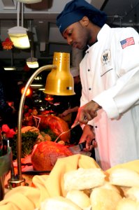 US Navy 111124-N-YC505-038 Culinary Specialist Seaman Aaron J. Hammond slices a ham on the mess decks aboard the aircraft carrier USS George H.W. B