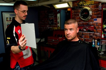US Navy 111128-N-RJ456-047 Ship's Serviceman Seaman Albert Sawyer shows Command Master Chief Stan Jewett his haircut in the barber shop aboard the