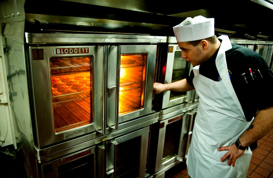US Navy 111211-N-GC412-437 Culinary Specialist Seaman Matthew Ryback checks on apple tarts in the oven in the bakeshop aboard the Nimitz-class airc