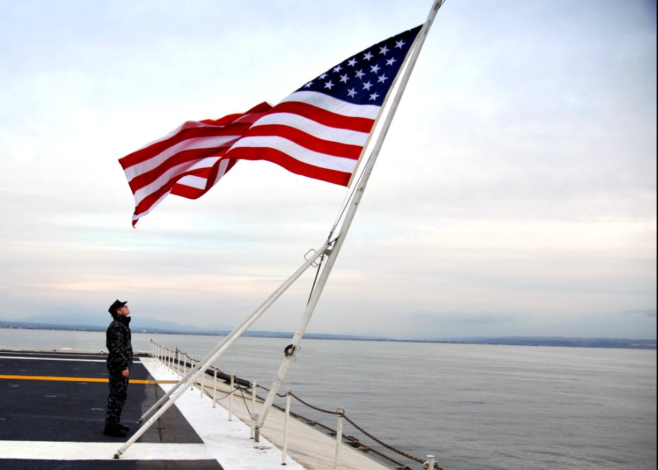 US Navy 111211-N-YB753-021 Quartermaster 3rd Class Shea Morgan faces the national ensign as the Nimitz-class aircraft carrier USS Abraham Lincoln (
