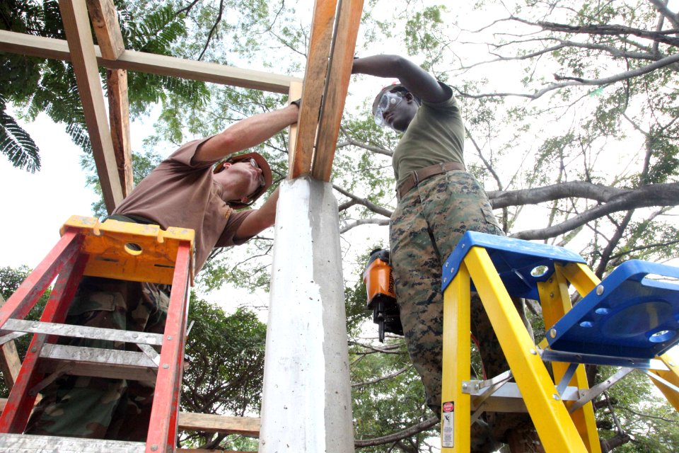 US Navy 111212-A-IP644-113 Builder 2nd Class Phillip Grindstaff and LCpl. Ronald Russell use a nail gun to steady rafters on an outdoor classroom b