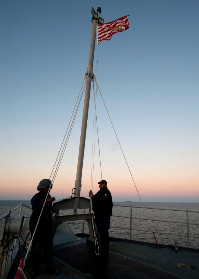 US Navy 111218-N-NR955-092 Hospital Corpsman 1st Class Darren V. Maxwell stands by to lower the Union Jack on the forecastle aboard the Whidbey Isl
