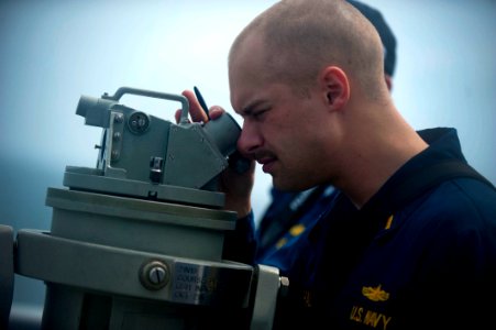 US Navy 111221-N-PB383-254 Ensign Benjamin Hall looks through a telescopic alidade to check the range of the Military Sealift Command fleet repleni