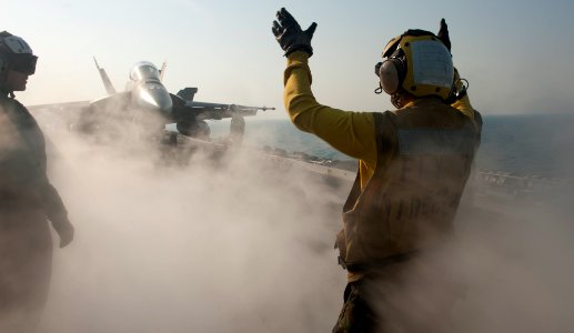 US Navy 111218-N-OY799-200 Aviation Boatswain's Mate (Handling) Airman Michael Linscott directs an F-A-18F Super Hornet from the Black Aces of Stri