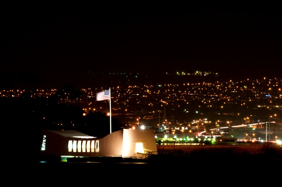 US Navy 111221-N-WP746-063 The national ensign flies above the USS Arizona Memorial at night with the lights of Pearl City, Hawaii in the backgroun