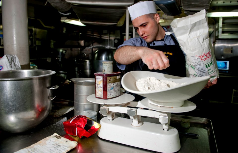 US Navy 111220-N-OY799-007 Culinary Specialist Seaman Matthew Ryback measures flour in preparation for the Christmas meal in the bake shop aboard t