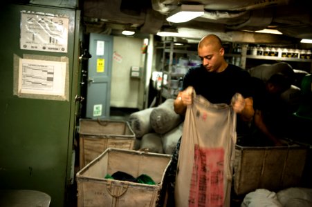 US Navy 120102-N-GC412-007 A Sailor fills a laundry bag with flight deck jerseys