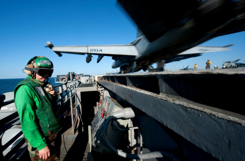 US Navy 120101-N-OY799-089 Aviation Boatswain's Mate (Equipment) 2nd Class Lian Lawrence stands waist safety as an F-A-18E Super Hornet from the To