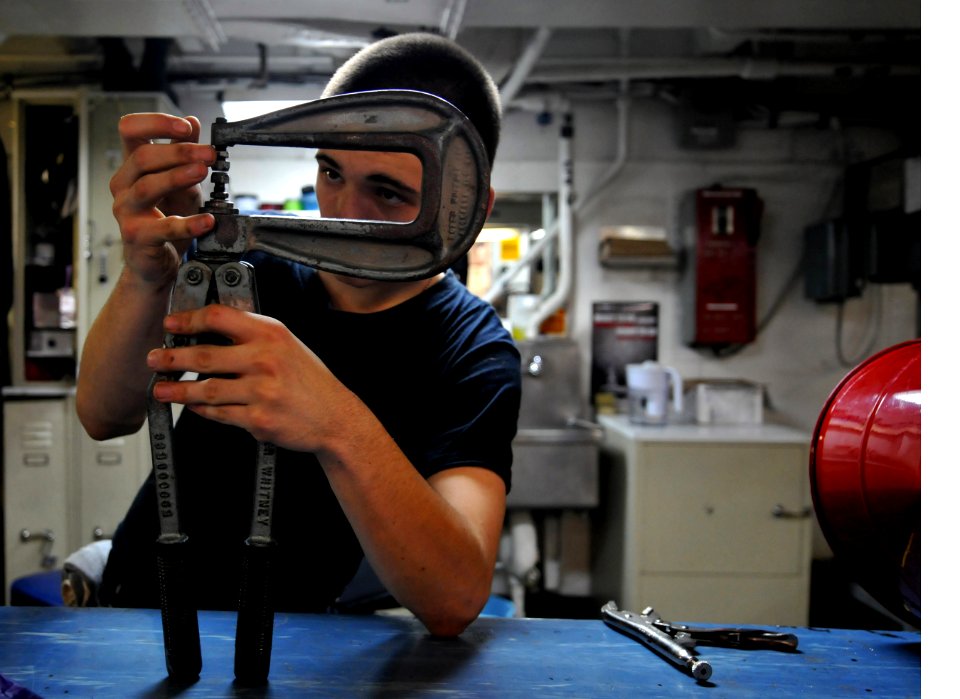 US Navy 120110-N-ZZ999-401 Airman Kaleb White adjusts a rivet squeezer while repairing a foreign object damage bucket