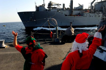 US Navy 111224-N-ED900-269 Sailors dressed as an elf and Santa Clause, assigned to the guided-missile destroyer USS Pinckney (DDG 91), wave the Mil